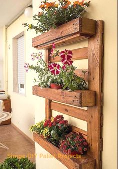 three wooden planters with flowers in them hanging on the side of a wall next to potted plants