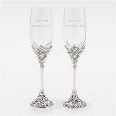 two crystal wine glasses sitting next to each other on a white surface with silver trimmings