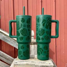 two green travel mugs sitting next to each other on a wooden table near a red wall