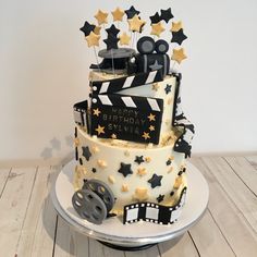 a birthday cake is decorated with black and gold stars, film claps, and the words happy birthday stella on it