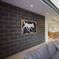 a grey couch sitting in front of a brick wall next to a kitchen and living room