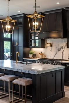 a kitchen with black cabinets and marble counter tops, two pendant lights hanging over the island