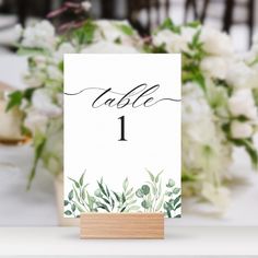 the table numbers are placed on top of each other, with greenery and white flowers in the background