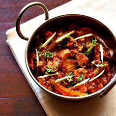 a pot filled with meat and vegetables on top of a wooden table next to a napkin