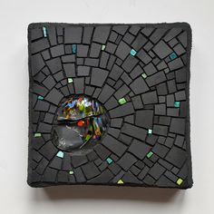 a black square with green and blue mosaic tiles on the surface, one half has a glass ball in it