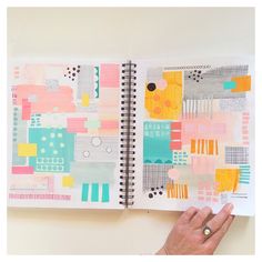 a hand holding a notebook open to a page with colorful art work on the pages