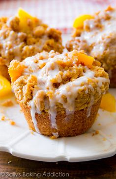 a muffin on a white plate topped with frosting and peaches next to another muffin