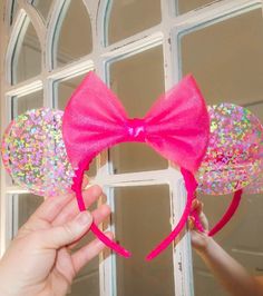 a person holding up a pink minnie mouse ears with sprinkles