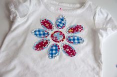 a white t - shirt with blue and red flowers on the front, sitting on top of a table