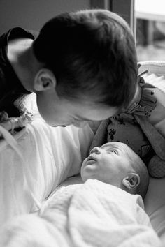 a woman kissing the nose of a baby laying on top of a bed next to a window