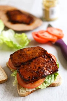 there is a sandwich with meat and lettuce on the table next to sliced tomatoes