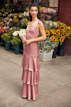 a woman standing in front of flowers wearing a pink dress with tiered ruffles