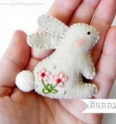 a hand holding a tiny stuffed animal in it's left hand with the word bunny brooch on it