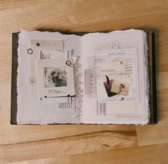 an open book on a wooden table with papers and other things inside the pages,