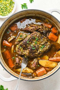 a pot filled with meat and vegetables on top of a white counter next to a spoon