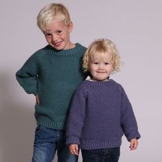 two young children standing next to each other wearing sweaters and jeans, smiling at the camera