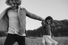 a man and woman are dancing in a field with mountains in the backgroud