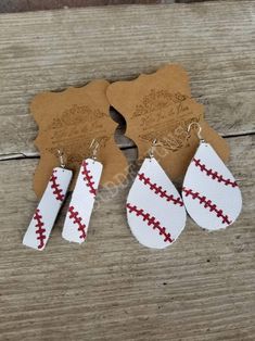 three pairs of white and red leather earrings on top of a wooden table next to a tag