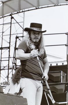 a man with long hair wearing a hat and holding a microphone while standing on stage