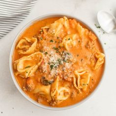 a white bowl filled with pasta and meat sauce on top of a table next to a spoon