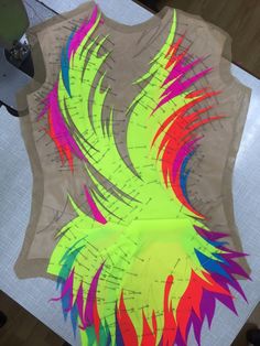 an image of a shirt with colorful feathers on it's chest and back, sitting on top of a piece of paper