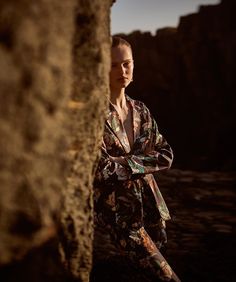 a woman leaning against a rock with her arms wrapped around her neck and legs crossed