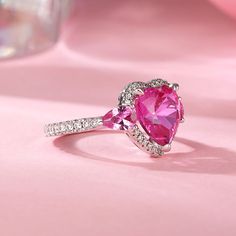 a pink heart shaped ring with diamonds around it