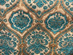 an ornate blue and gold design on a piece of fabric with some light brown highlights