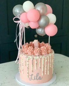 a pink cake with balloons on top and the word ella spelled in silver, white, and pink icing