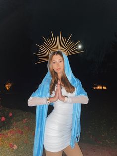 a woman in a white dress and blue shawl is standing with her hands together