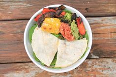 a white bowl filled with vegetables and tortilla wrap on top of a wooden table