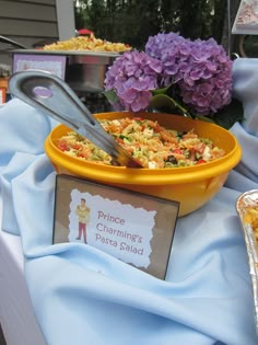 a yellow bowl filled with food on top of a blue table cloth next to purple flowers