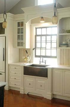 a kitchen with white cabinets and wood flooring next to an open window that looks out onto the outdoors