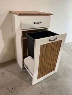 a white cabinet with two drawers and a trash can in it's bottom drawer