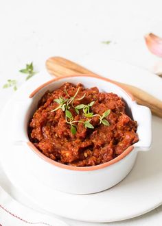 a white bowl filled with chili on top of a plate next to wooden spoons