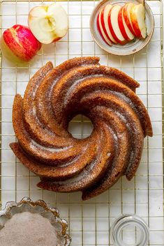 an apple bundt cake on a cooling rack next to two bowls with apples in them