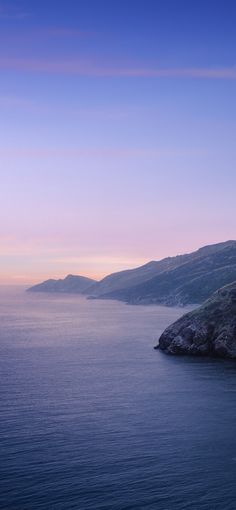 a lighthouse on top of a cliff overlooking the ocean at sunset or dawn with mountains in the distance