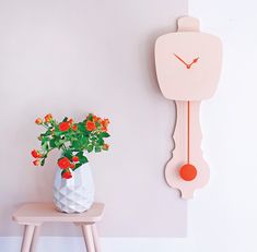 a white vase filled with flowers next to a pink clock on the side of a wall