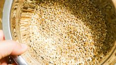 a person holding a spoon over a bowl filled with sesame seeds