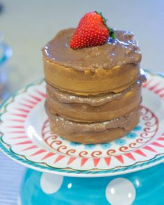 a stack of pancakes with chocolate frosting and a strawberry on top, sitting on a polka dot plate