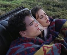 a man and woman laying in the grass under a blanket on a couch with their eyes closed