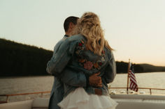 a man and woman standing on the back of a boat looking at the water with an american flag in the background