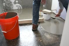 a person standing next to a red bucket on the floor in front of a mirror