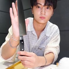 a man holding up a large knife on top of a white table next to a gold box