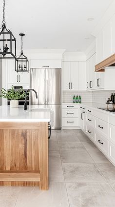 a large kitchen with white cabinets and wooden island in the center, surrounded by potted plants