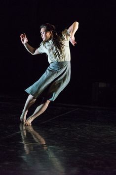 a woman is dancing in the dark with her arms spread out and one leg bent