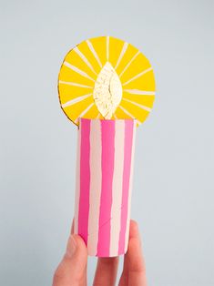 a hand holding up a paper cup with a yellow and pink decoration on it's side