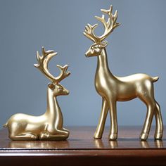 two gold deer figurines sitting on top of a wooden table next to each other