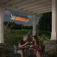 a man and woman sitting at a table under an outdoor heater on a patio