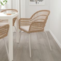 two wicker chairs sitting on top of a wooden floor next to a white table